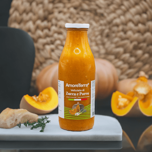 Una scena calda e autunnale con la vellutata di zucca e porro AmoreTerra in bottiglia di vetro, affiancata da fette di zucca fresca e rosmarino. Perfetta per trasmettere naturalità e genuinità.
